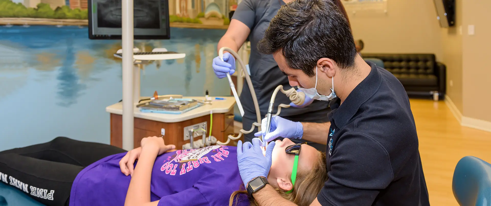 At Star Smile Orthodontics in Bloomingdale IL, a dentist examines a patient's mouth while an assistant operates a suction device; the patient reclines in the dental chair wearing sunglasses.