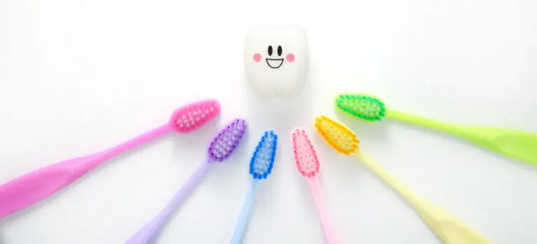 A rainbow of toothbrushes surround a smiling tooth for a blog post about choosing the right pediatric dentist