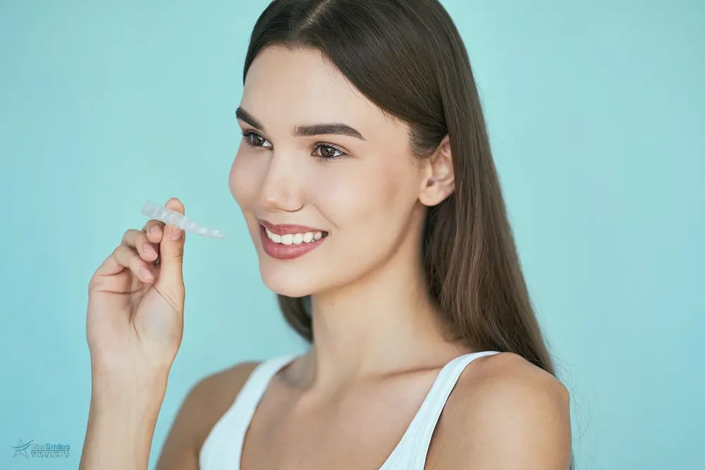 a woman smiling and holding Invisalign wondering about Invisalign cost in Bloomingdale and Naperville, IL