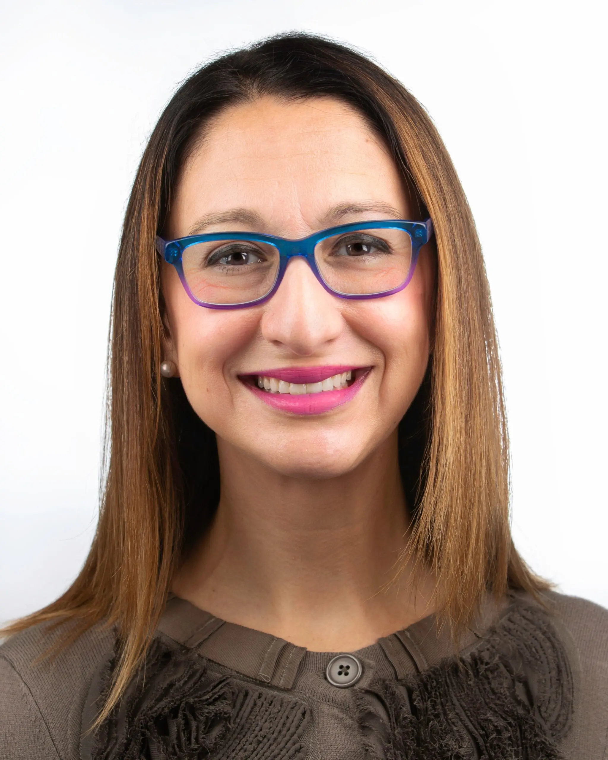 Smiling against a plain white background, a woman with straight brown hair, blue glasses, a brown textured top, and pink lipstick represents the expert team at Star Smile Orthodontics in Bloomingdale IL, where board-certified orthodontist MsD provides exceptional care.