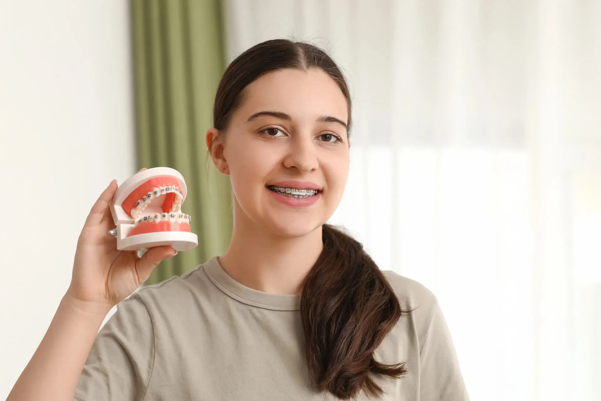 A young woman with braces smiles and holds a dental model featuring metal braces, representing Star Smile Orthodontics in Bloomingdale, IL.
