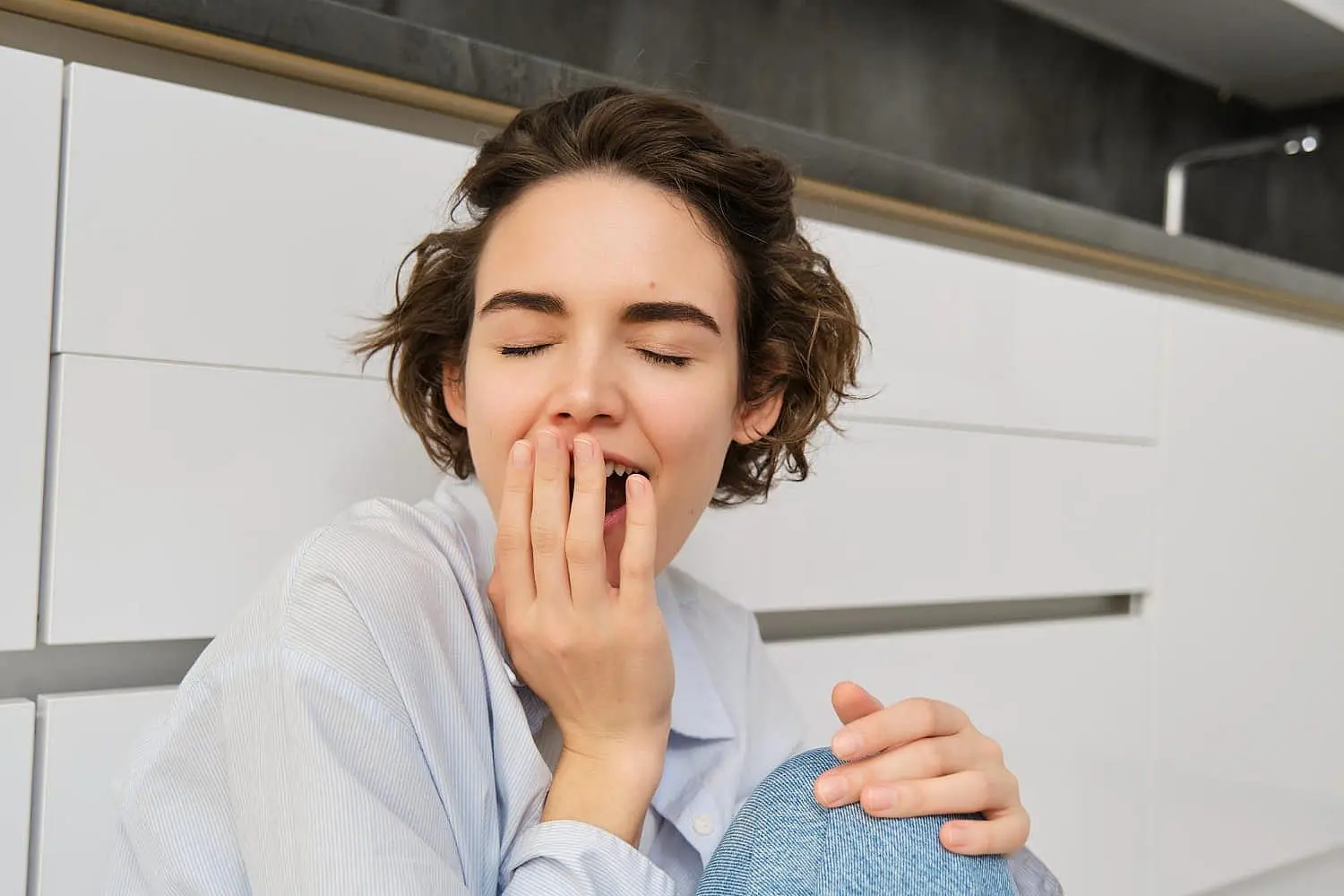 A woman in a white shirt yawns, revealing his tendency as a mouth breather, while covering his mouth against a white background in Bloomingdale and Naperville, IL.