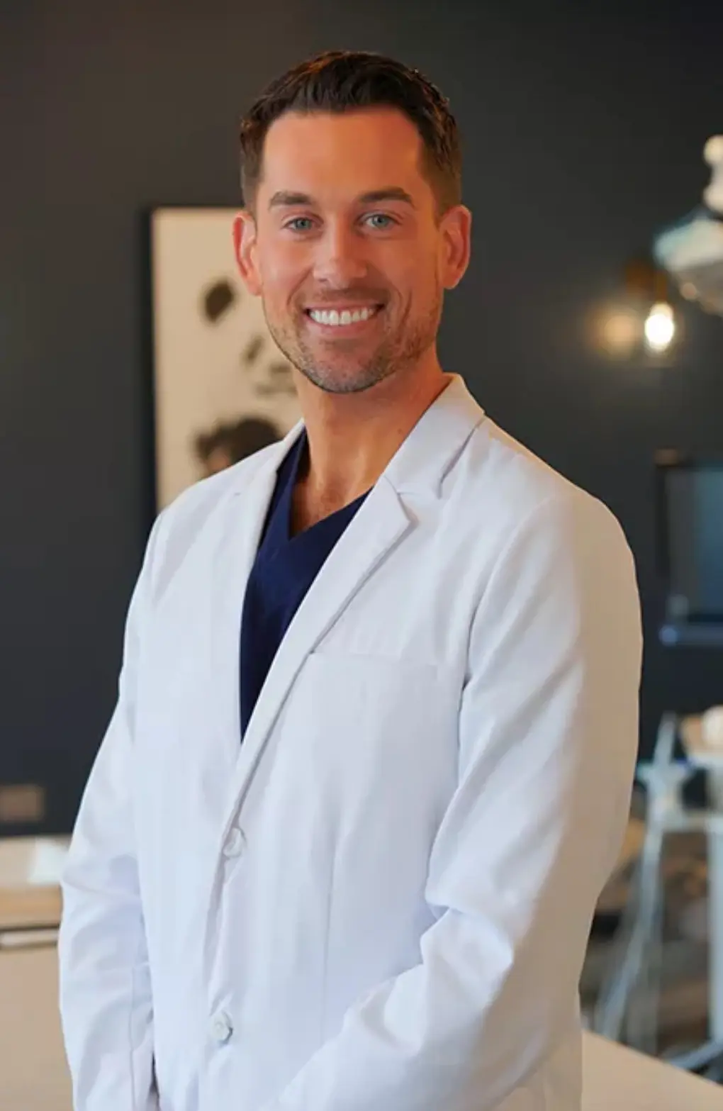 At Star Smiles Pediatric Dentistry in Bloomingdale or Naperville, IL, Dr. Deric Truskoski, DMD, MS, is pictured indoors wearing a white lab coat and smiling at the camera against a neutral background.