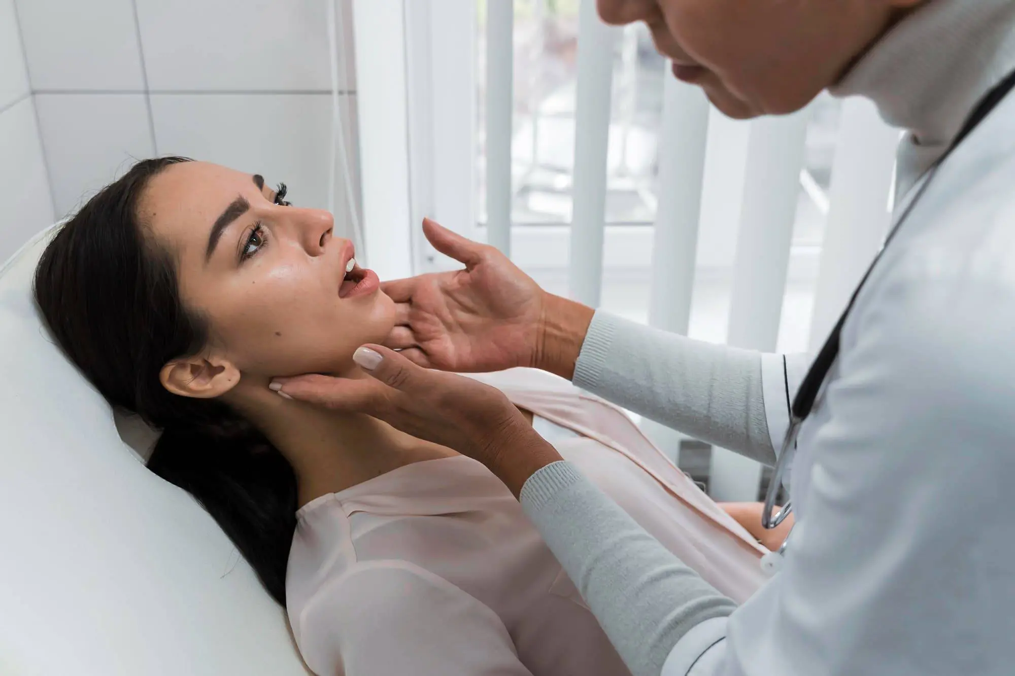 A doctor checks the throat of a seated female patient, discussing about jaw surgery options in a modern medical office in Bloomingdale and Naperville, IL.