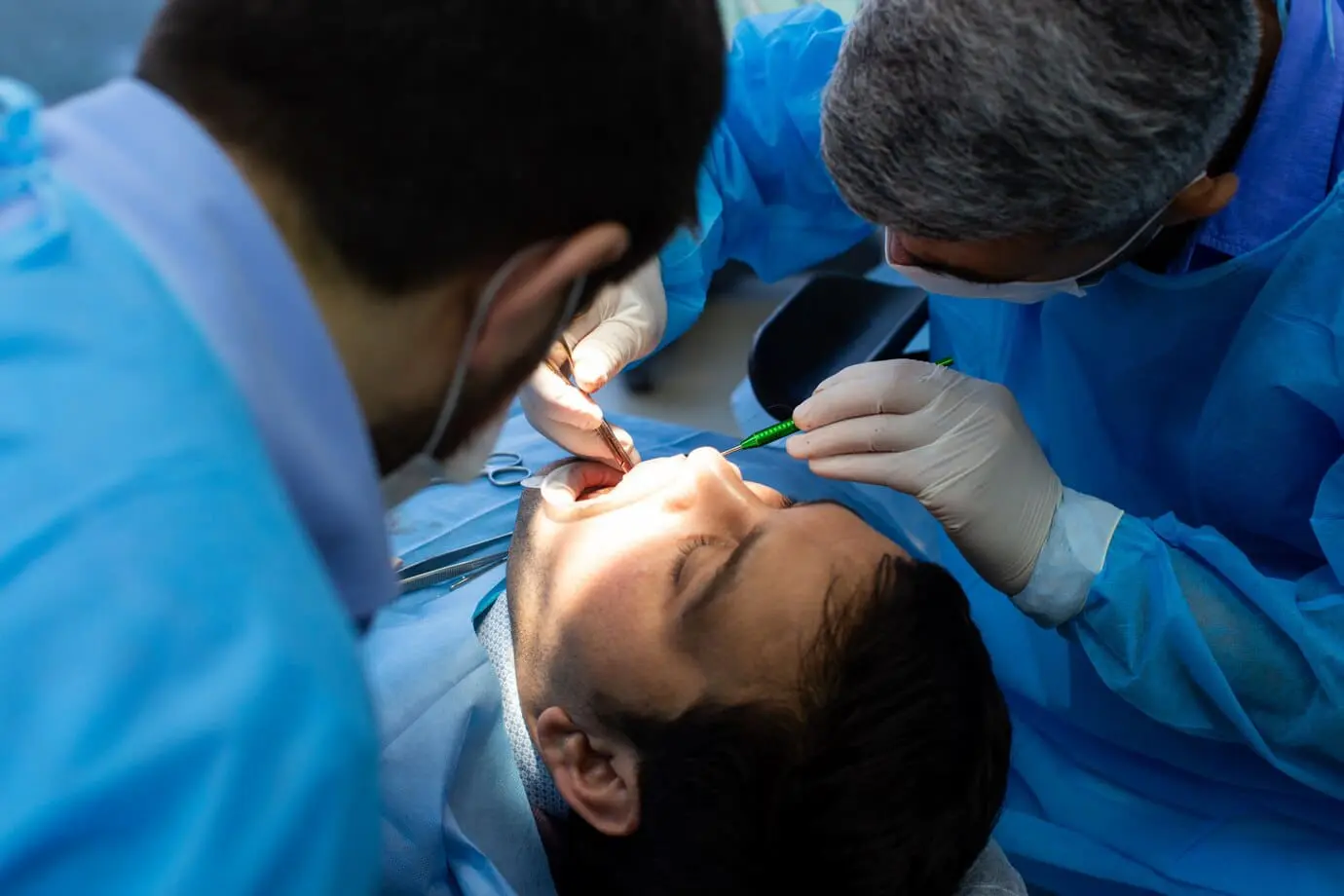 Two dentists in blue scrubs perform a dental procedure on a patient lying on an examination chair with problem tongue thrust in Bloomingdale and Naperville, IL.