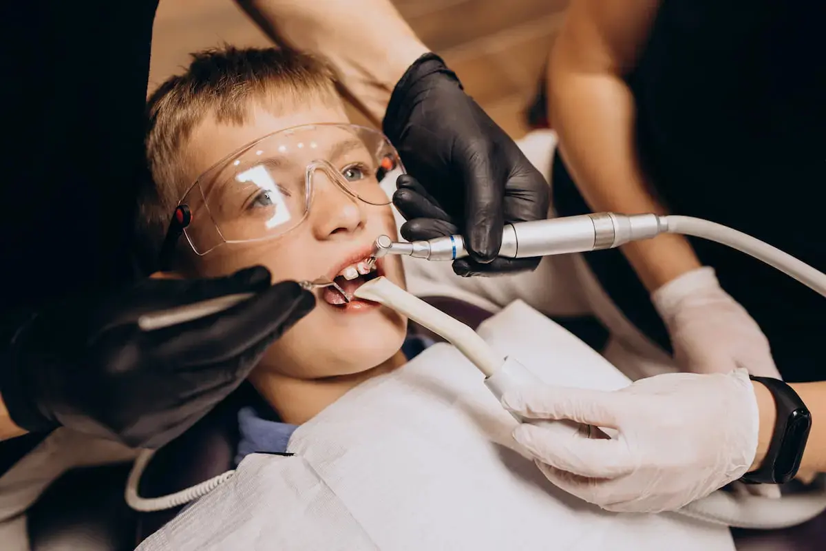 In a well-equipped clinic known Star Smiles Orthodontics and Pediatric Dentistry, a dentist examines a young boy sitting in a dental chair, her mouth open and shielded by a protective bib in Bloomingdale, IL.