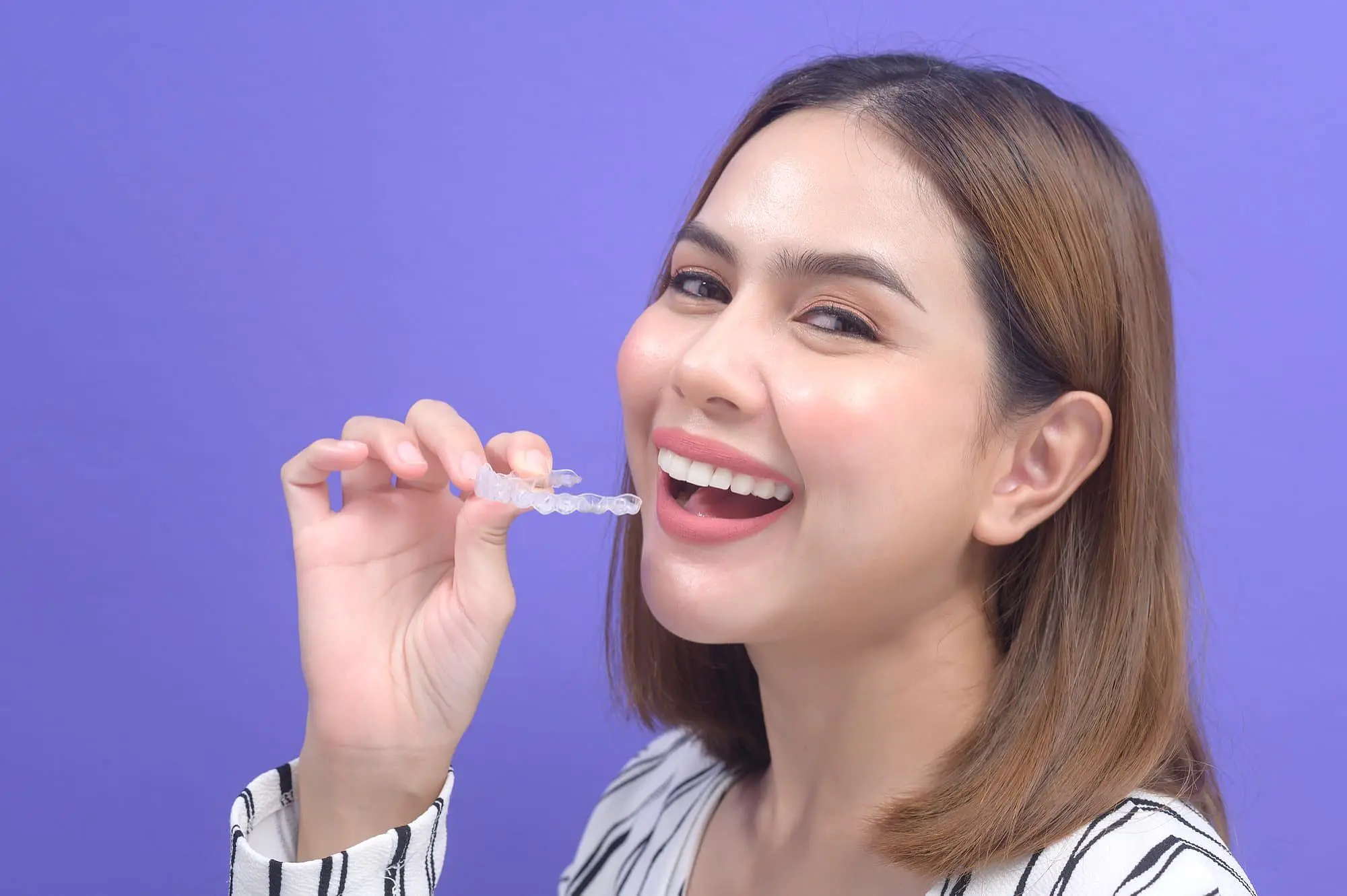 A smiling woman holds a clear dental retainer from Invisalign in her hands when choosing a Invisalign payment plan in Bloomingdale and Naperville, IL.