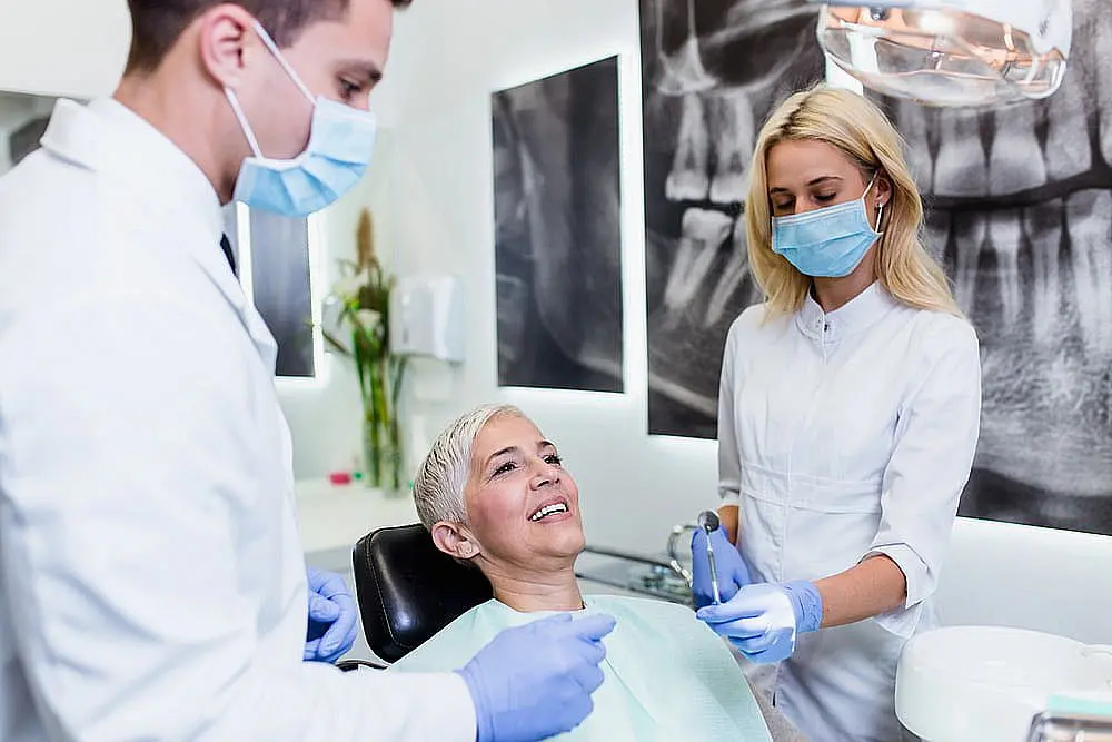 A woman smiles in a modern dental chair as two masked and gloved dental professionals prepare tools for her adult orthodontics treatment at Star Smiles Orthodontics and Pediatric Dentistry in Bloomingdale and Naperville, IL.