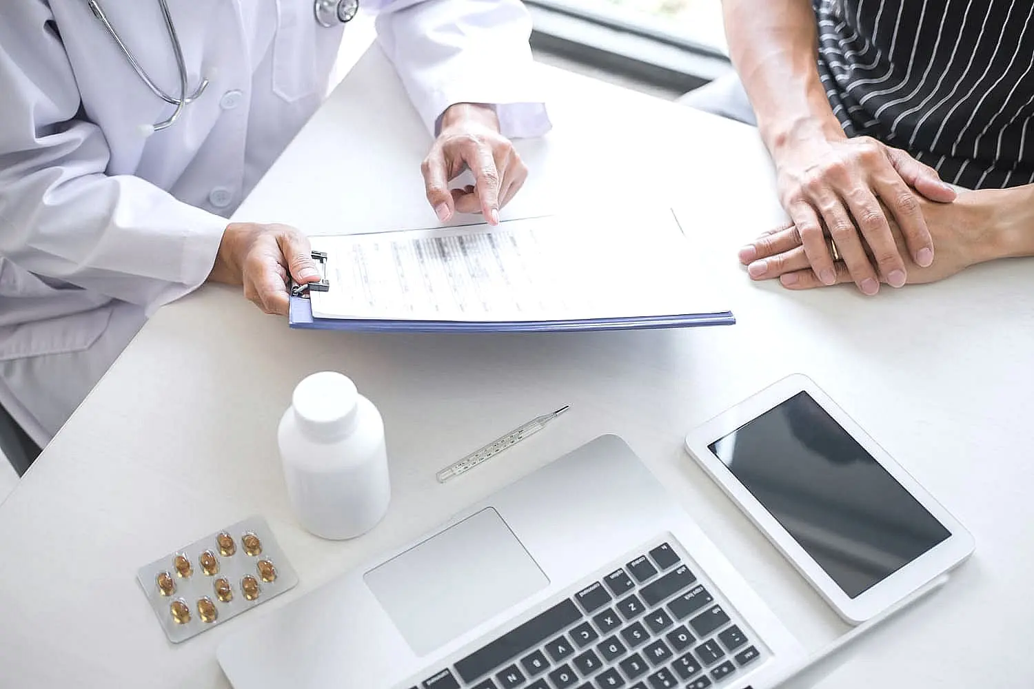 A dentist discusses orthodontic insurance plans with a patient at a desk, reviewing paperwork alongside a laptop, tablet, and medication on the table in Bloomingdale and Naperville, IL.