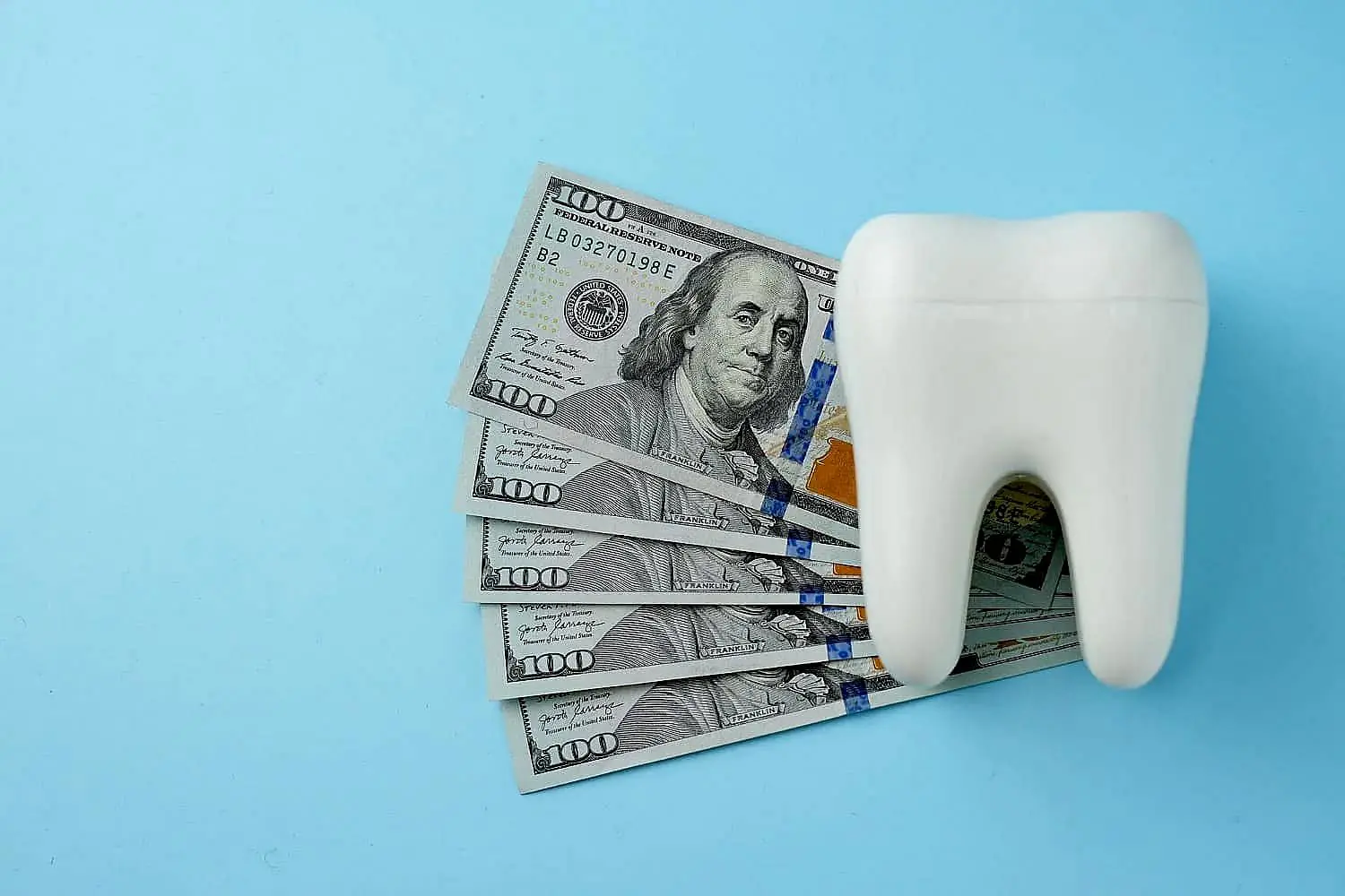 A large model of a tooth is placed beside several 100-dollar bills on a blue background, subtly hinting at the cost-effectiveness of an Invisalign payment plan in Bloomingdale and Naperville, IL.
