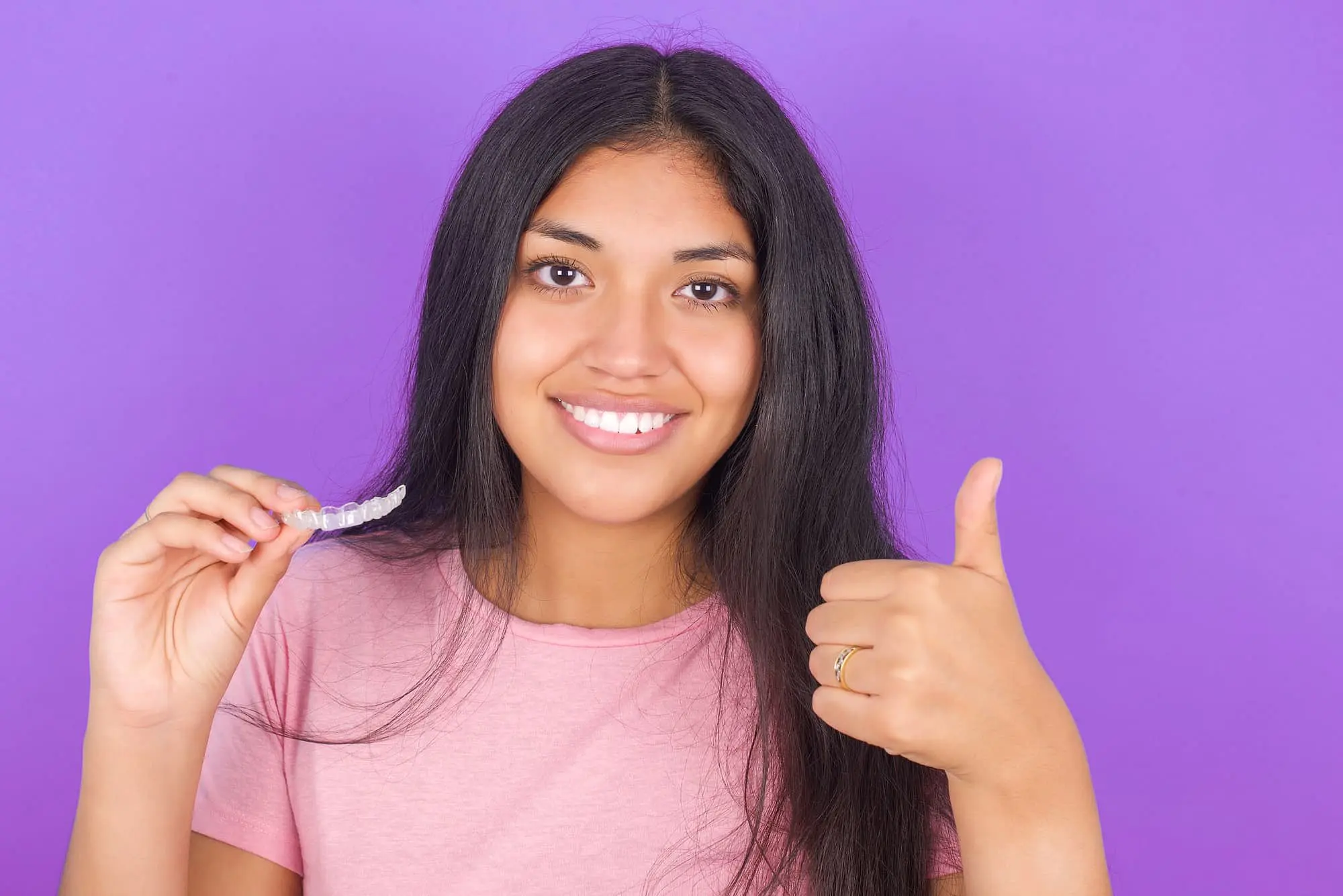 Woman in a pink clothes holding a clear dental aligner, happy with Invisalign payment at Star Smiles Orthodontics and Pediatric Dentistry in Bloomingdale and Naperville, IL.