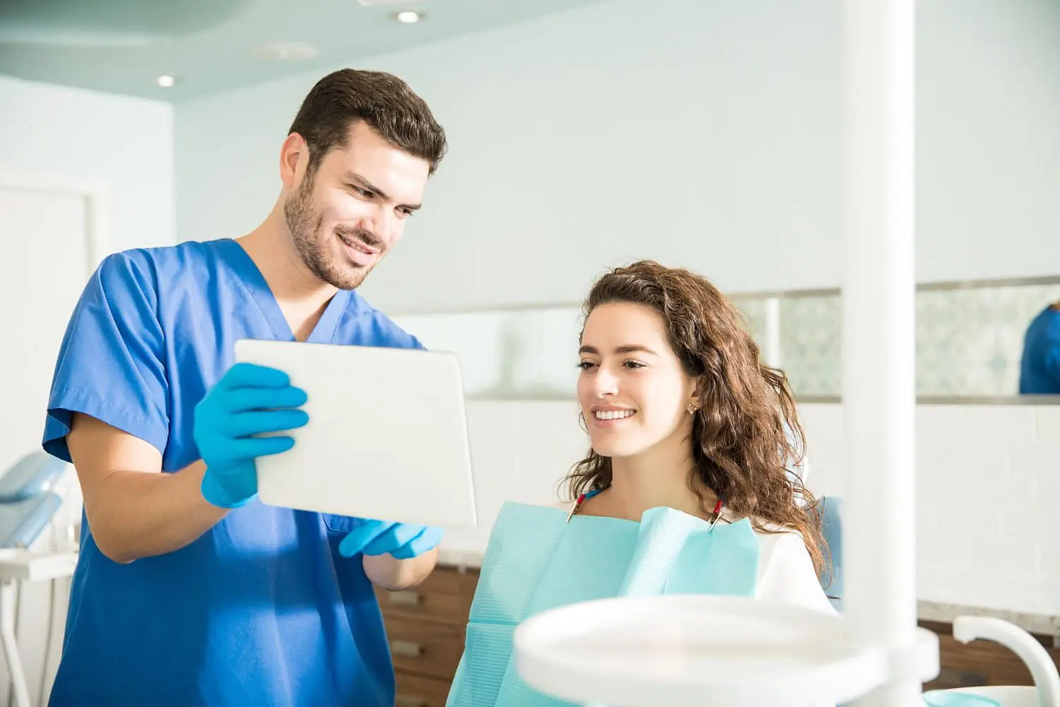 Adult dentist showing digital tablet to female patient for reviews orthodontic insurance plans with a patient in the clinic in Bloomingdale and Naperville, IL.