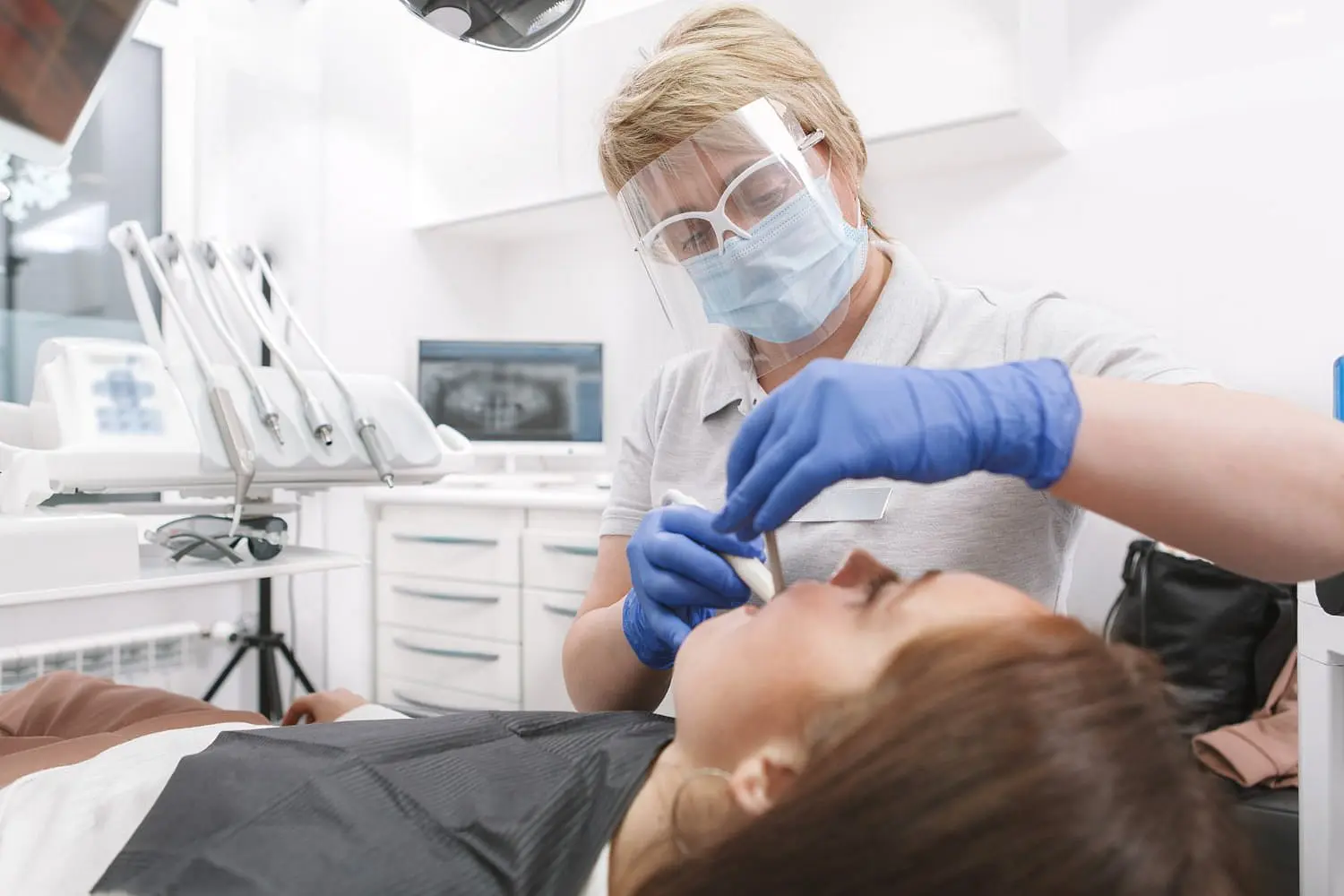 Person receiving dental braces check-up by dentist with a gloved hand holding dental instruments near their mouth from top-rated orthodontist in Bloomingdale, IL.