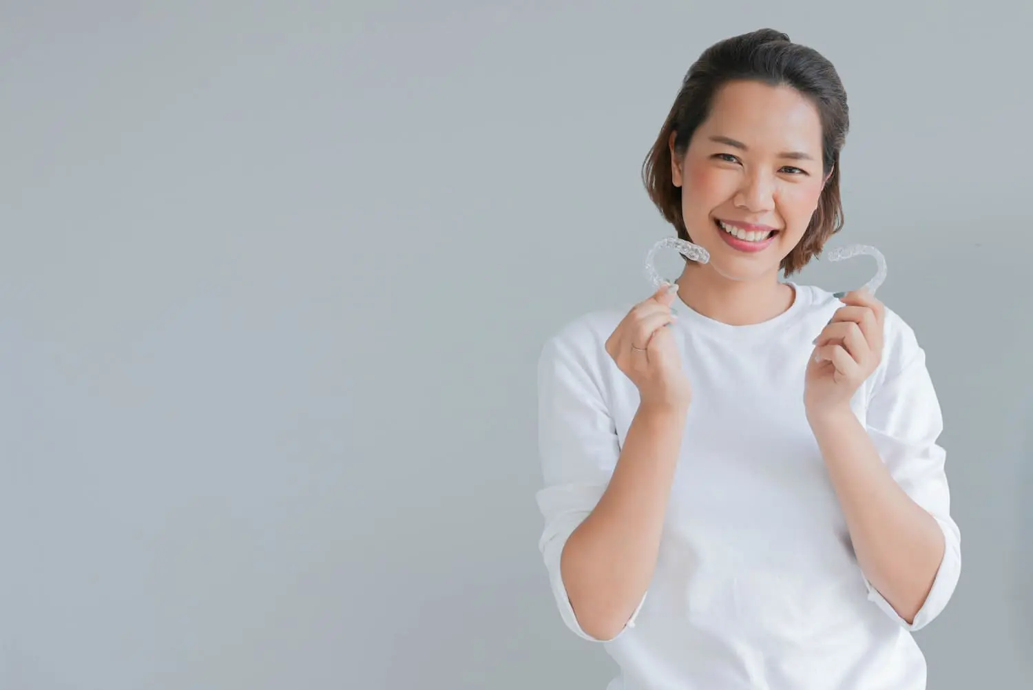 Young woman smiling with holds dental aligner from Invisalign at Star Smiles Orthodontics and Pediatric Dentistry in Naperville, IL.