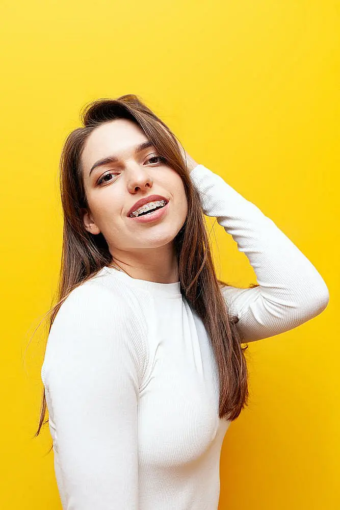 Close-up of a woman smiling with ceramic braces on their teeth, wearing a white clothes in Naperville, IL.