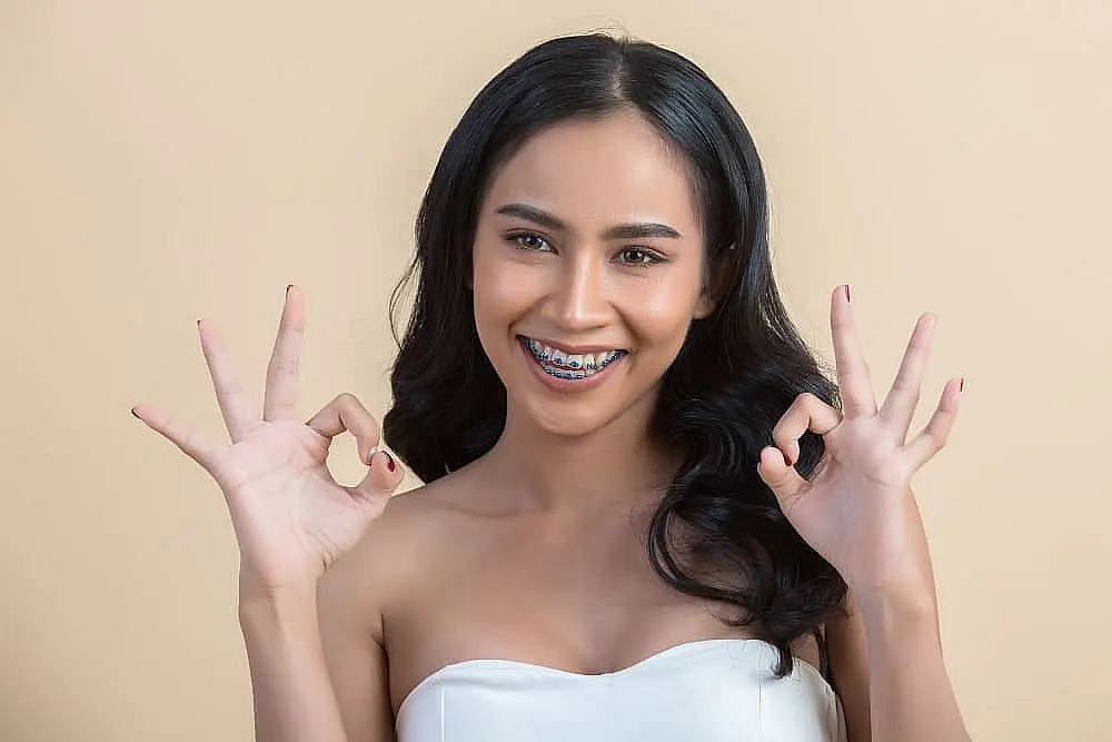 A woman with long black hair and metal braces smiles, making hand gestures against top-rated orthodontist at Star Smiles Orthodontics and Pediatric Dentistry in Bloomingdale and Naperville, IL.