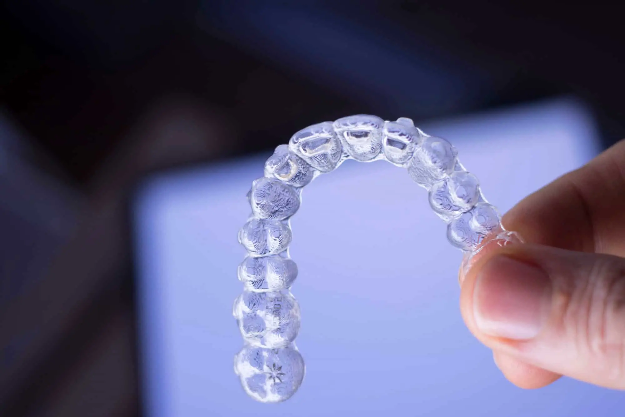 A hand holds Invisalign clear aligner against a blue background show Star Smiles Orthodontics and Pediatric Dentistry provide cheap Invisalign cost in Bloomingdale and Naperville, IL.