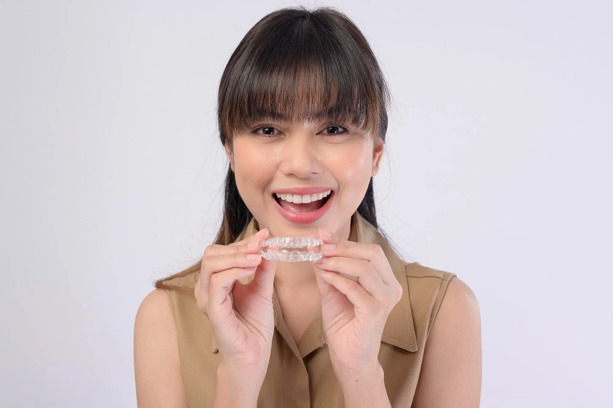 A woman smiling and holding a clear dental aligner near her face, show invisalign insurance covered from Star Smiles Orthodontics and Pediatric Dentistry in Bloomingdale and Naperville, IL.