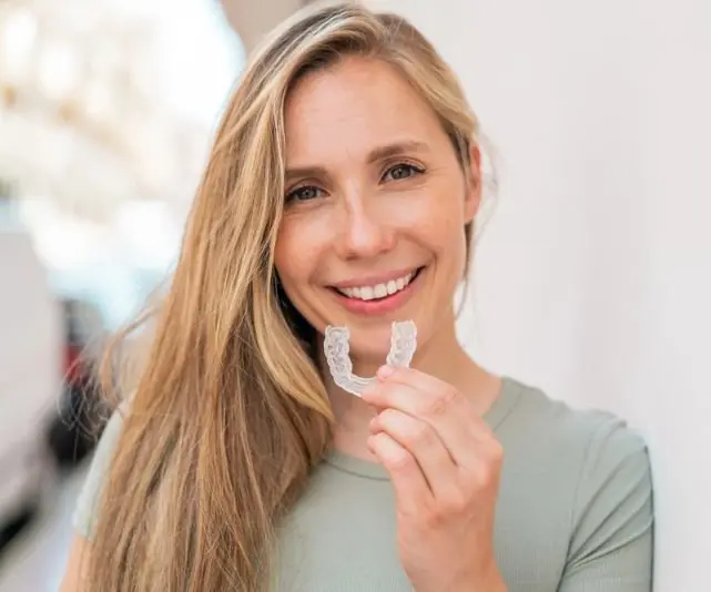A woman holds a clear dental aligner Invisalign from trusted orthodontist in Bloomingdale, IL.