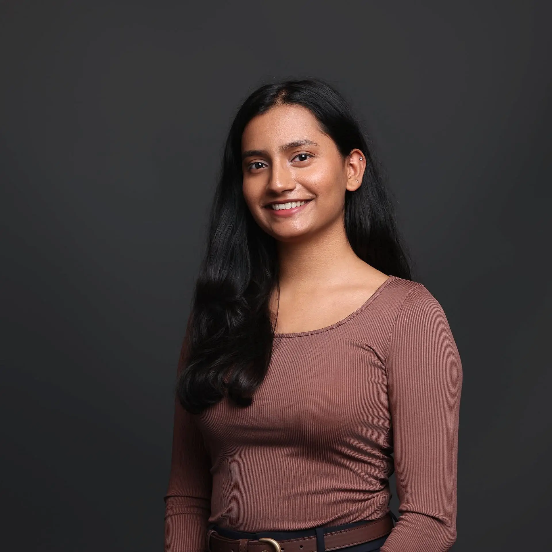 Dr. Saloni Patel is Pediatric Dentist at Star Smiles Pediatric Dentistry in Bloomingdale or Naperville, IL—recognized by her long black hair and brown long-sleeve top—smiles warmly against a dark background.