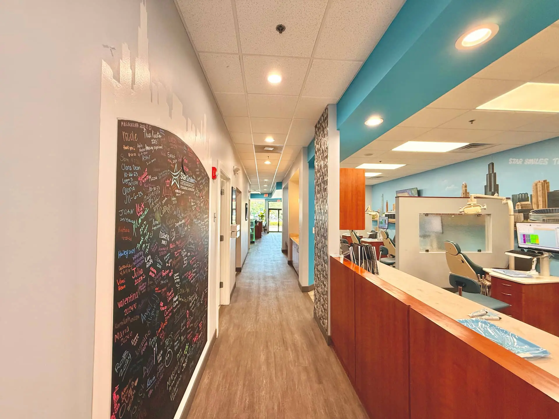 At Star Smiles Orthodontics & Pediatric Dentistry in Bloomingdale or Naperville, IL, a brightly lit hallway features a large blackboard filled with colorful writing on the left and a reception desk on the right.
