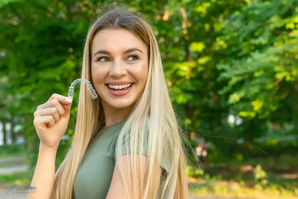 beautiful smiling woman holding invisalign clear aligners - Invisalign vs Braces Cost in Bloomingdale and Naperville, IL. 