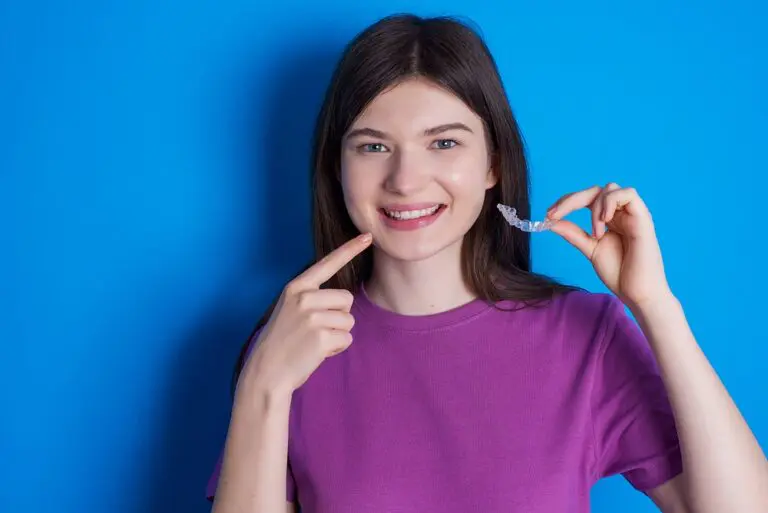 A woman in a purple shirt points to her teeth and holds an aligner, showing Star Smiles Pediatric Dentistry Can Invisalign Fix Overbite in Bloomingdale or Naperville, IL.
