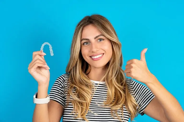 young beautiful woman blonde holding invisalign clear aligners blue studio background - Aligners vs Braces in Bloomingdale and Naperville, IL