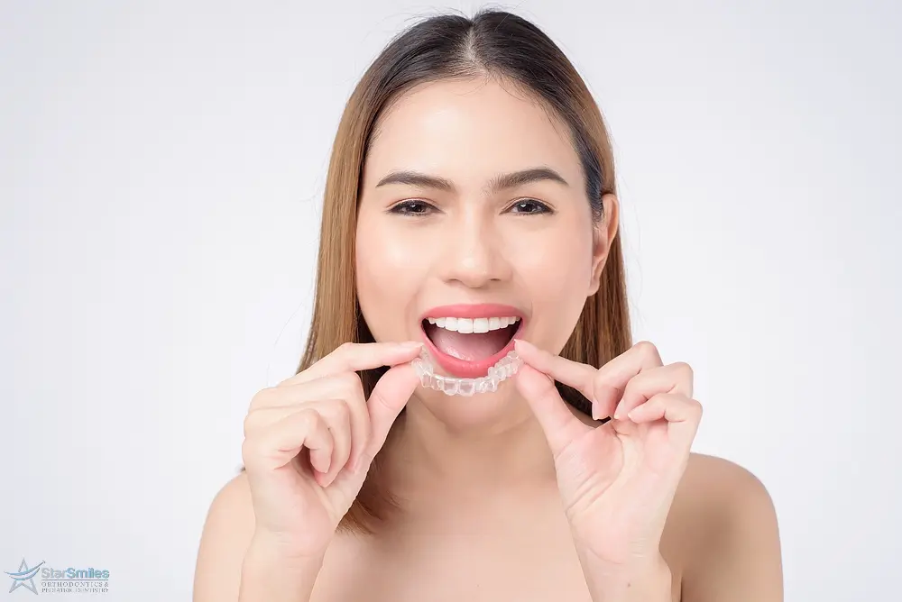 young smiling woman holding invisalign clear aligners studio dental - How Long Does Invisalign Take in Bloomingdale, IL