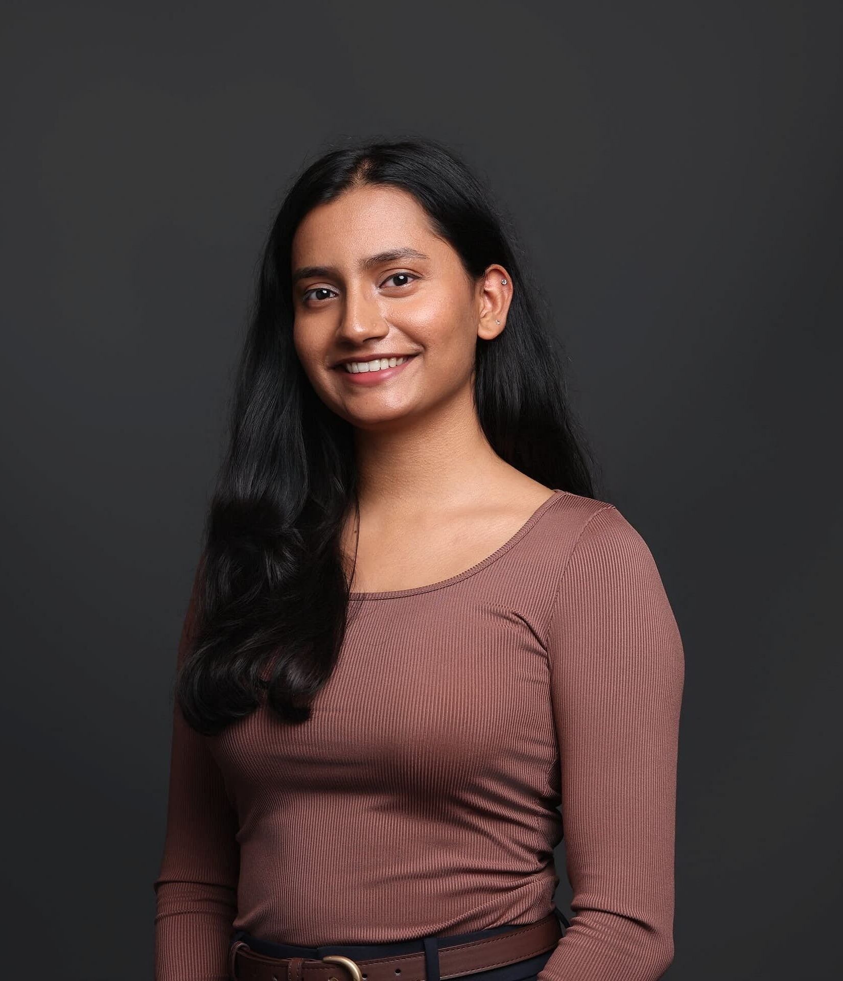At Star Smiles Pediatric Dentistry in Bloomingdale or Naperville, IL, Dr. Saloni Patel—recognized by her long black hair and brown long-sleeve top—smiles warmly against a dark background.